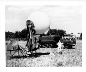 Black and white archival photo of a military balloon near Army truck with person standing in front of truck.
