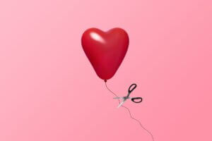 Heart shaped red balloon floating while attached to a string which is about to be cut by free-floating scissors.