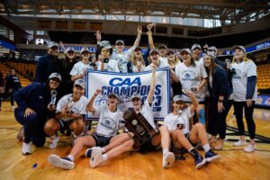 Women's basketball tam members celebrating on court with banner