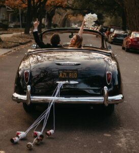 Groom and bride in old fashioned car with cans tied to car bumper with string