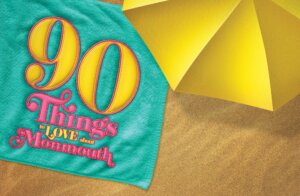 Illustration of beach towel with "90 Things to Love about Monmouth" embroidered. Towel is partially covered by beach umbrella