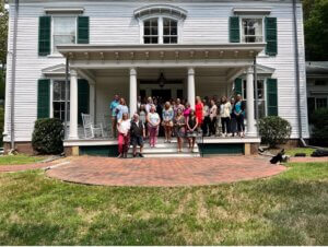 Group of students and professors standing on the porch of a historic home.