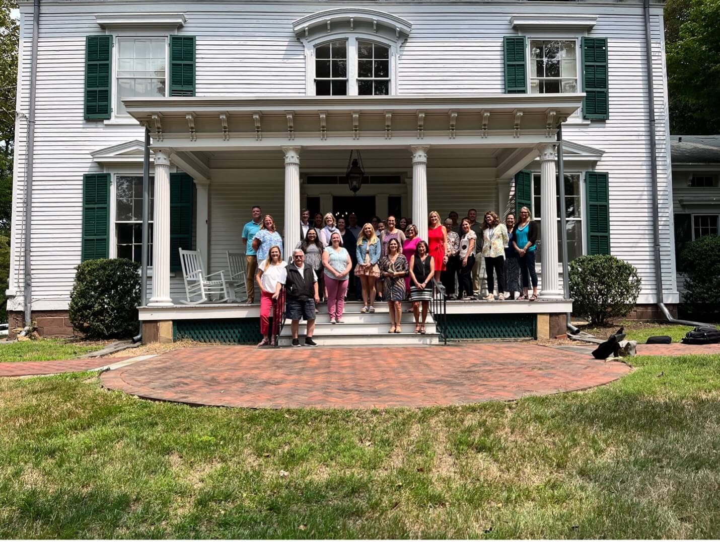 Group of students and professors standing on the porch of a historic home.