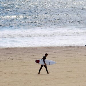 Photograph of person in silhouette walking parallel to the edge of ocean while holding a surfboard