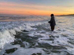 Man casting fishing rod into sea while standing at shoreline