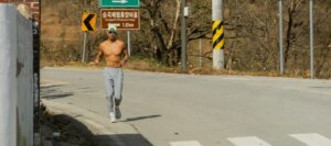 Shirtless man running on paved road in front of traffic sign in Korean