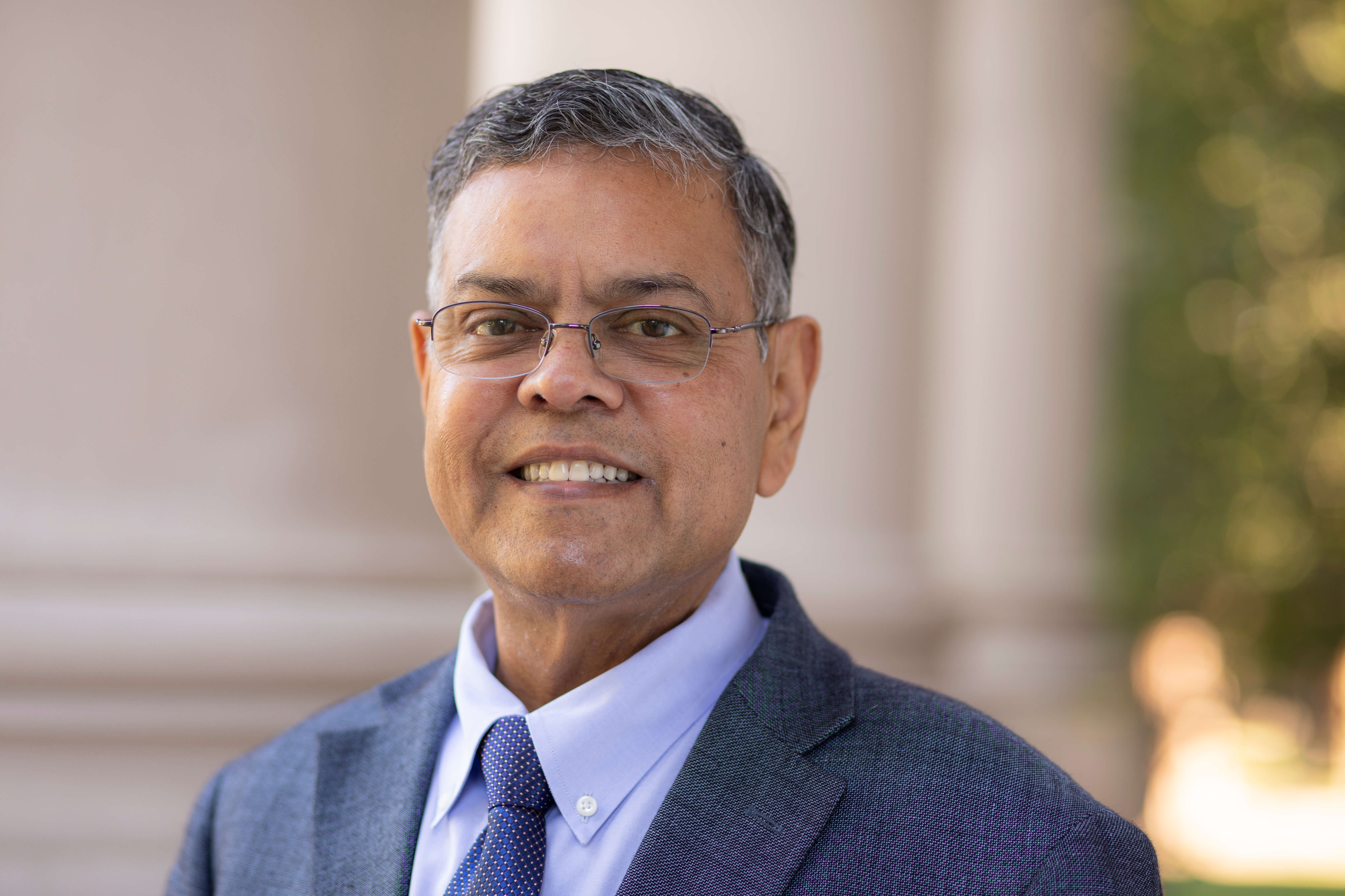 Headshot of Dean Raj Devasagayam standing in front of the Great Hall at Monmouth University