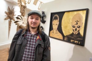 Monmouth University student Tyler Bane posing in front of the Cardboard Show gallery at Rechnitz Hall.