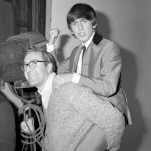 Vintage black and white image of George Harrison climbing on the back of Mal Evans