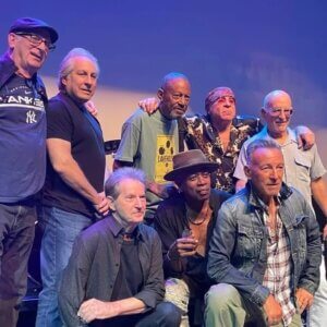 musicians surround Bruce Springsteen, who is kneeling on stage