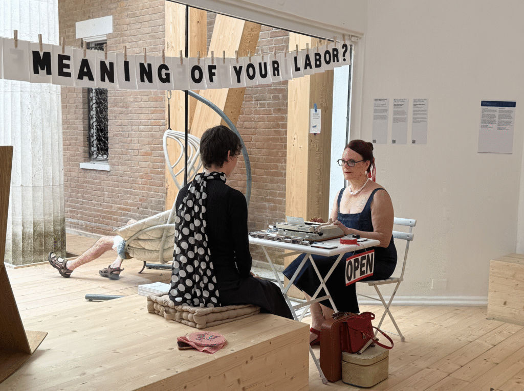 A woman seated at a typewriter takes dictation from another woman.