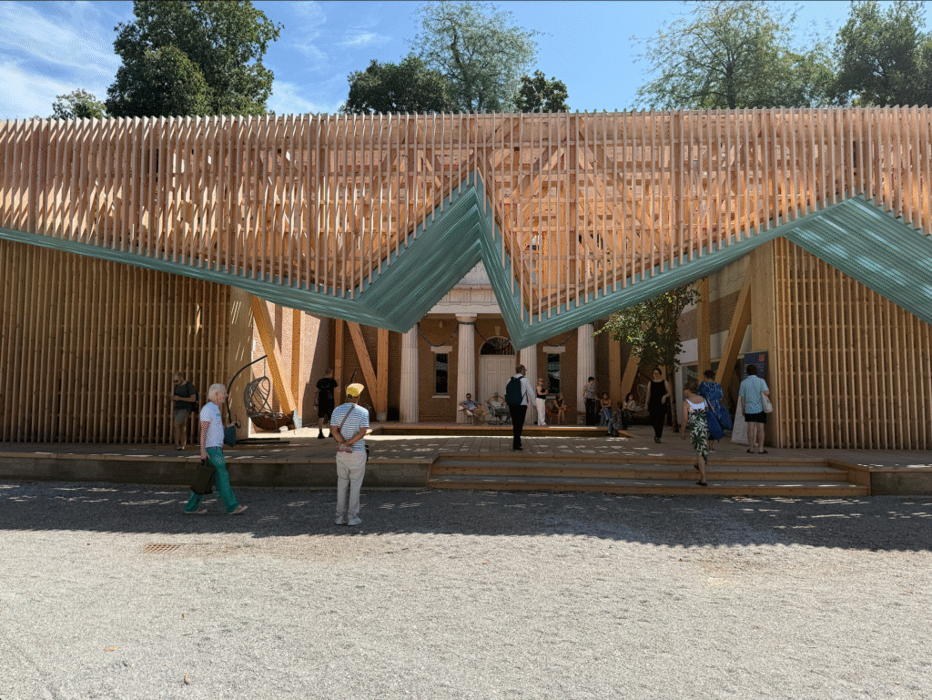 A wooden geometric structure of bare wood with blue on the bottom provides a porch covering for the Neoclassical-styled US Pavilion in Venice Biennial.