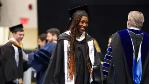 A smiling female student in academic regalia at a commencement ceremony