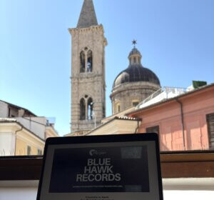 Italian city skyline in background, with Blue Hawk Records sign in foreground
