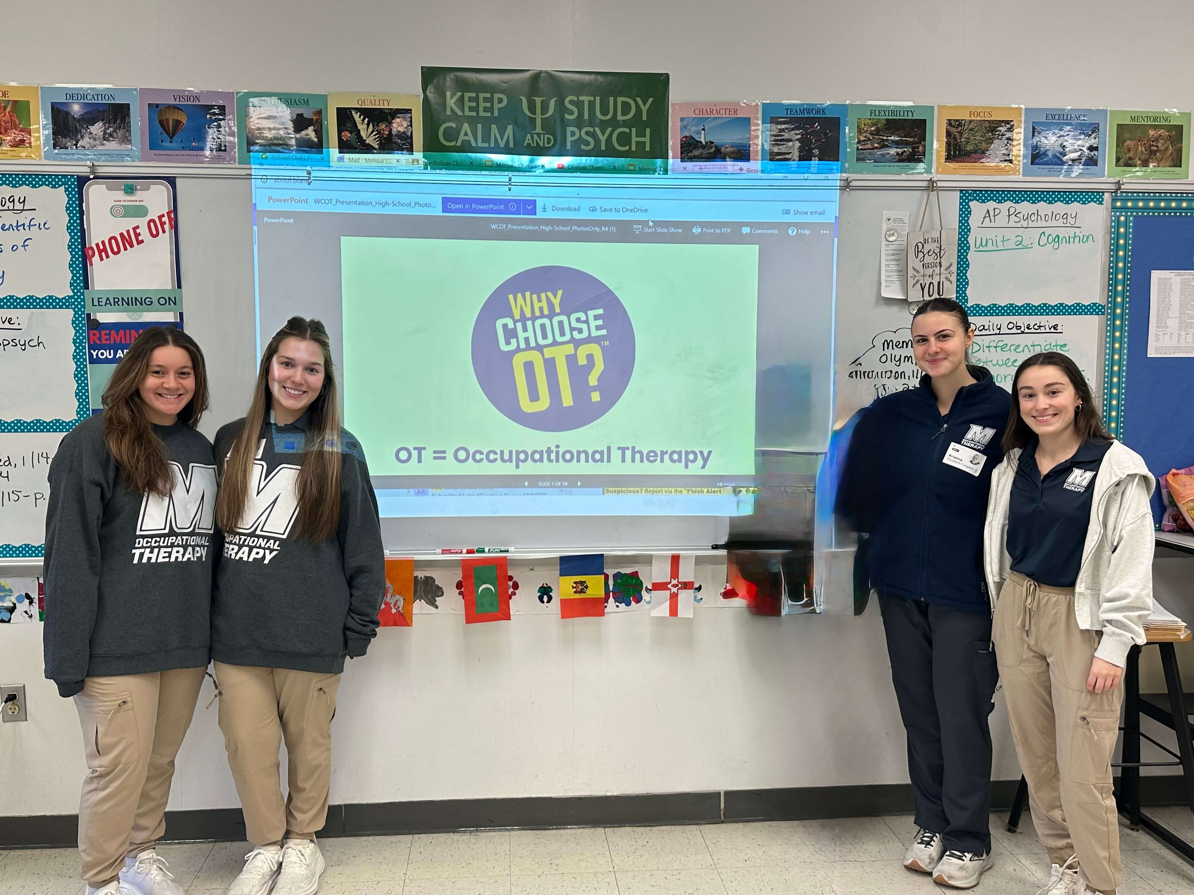 Four female students wearing Monmouth University clothing stand in front of a presentation about choosing Occupational Therapy