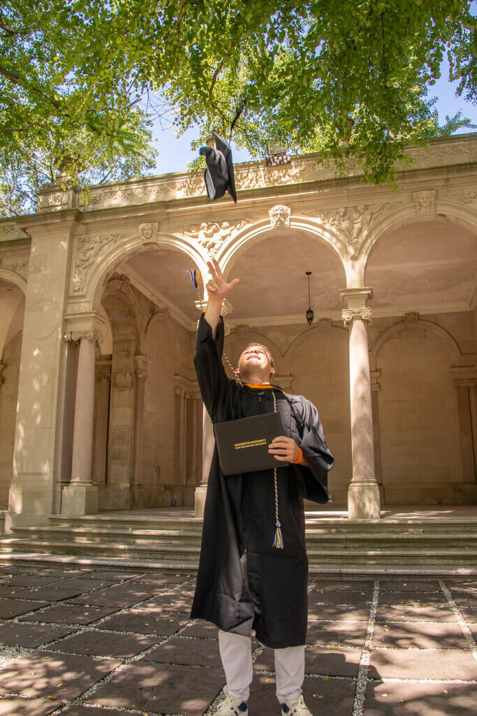 A student in a graduation gown throws his cap in the air