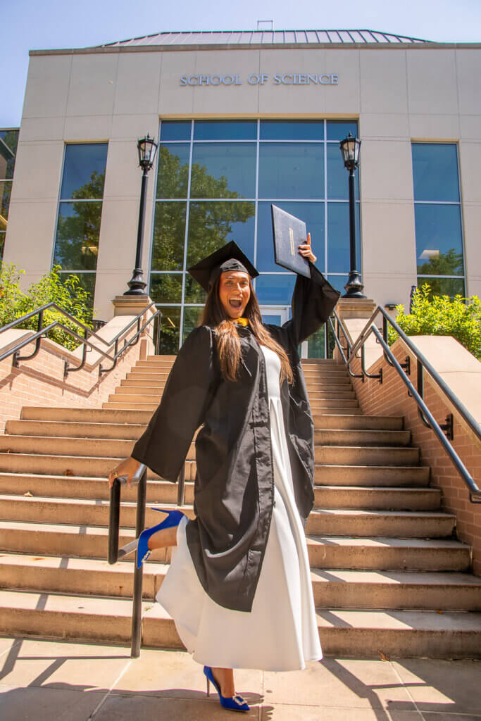 A student in graduation cap and gown holds up her diploma