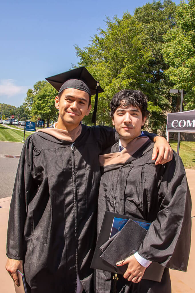 Two students in graduation gowns pose for a photo