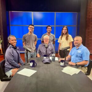 Tim Thompson (center) sits around a desk with students and an industry professional in a podcast studio