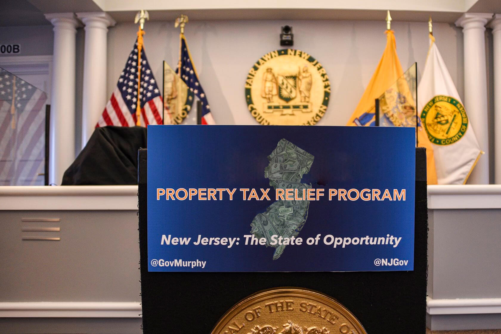 Image of podium with sign that reads. Property tax Relief Program , New Jersey the state of opportunity.