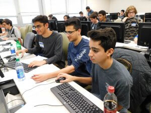 3 male students in front of a group of male and female students working on their programs