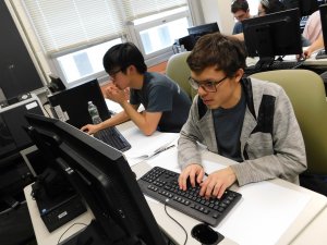 2 male students, 1 typing and 1 using their mouse, working on their computers