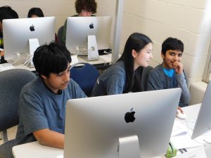 1 female student smiling and sitting in between 2 male students at the competition