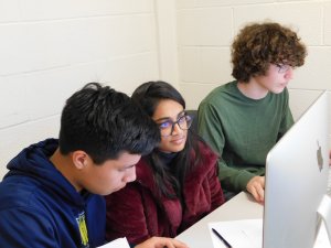 1 female student sitting in between 2 male students at the competition