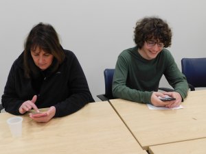 High School teacher Susanne Signorelli and student sitting at table and looking at their phones