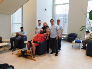 5 male students, one with a golden retriever service dog, and professor smiling for the camera