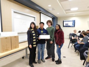 3 students (2 males and 1 female) with their teacher Ms. Corrado holding up a 3D printer they each won for 1st place in the Monmouth University High School Programming Contest