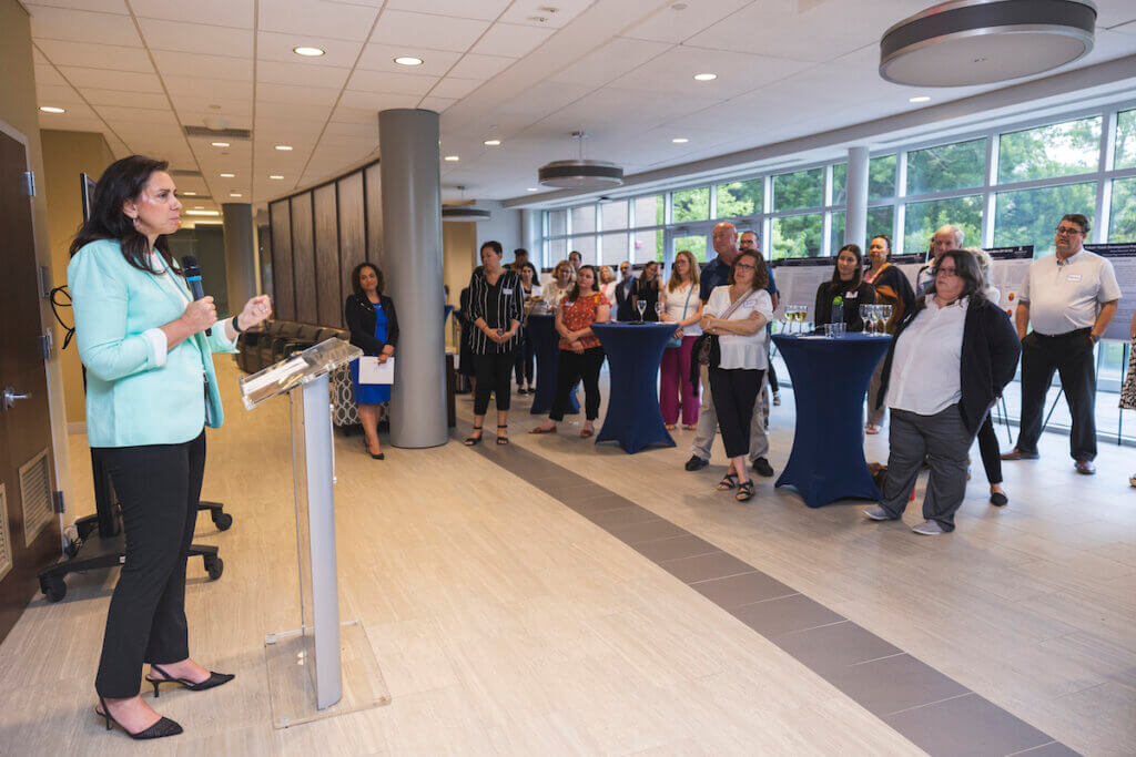 Crowd of professionals listen intently as fellow professional speaks at podium