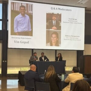 Two men and a woman sitting on a panel in front of a screen that reads "New Jersey Senator Vin Gopal"