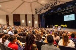 A packed audience in an auditorium watching a stage with two people talking in chairs.