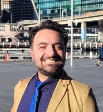 Man in suit and tie smiling outside of a large building.