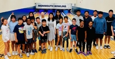 group of 30 or so camp participants posing for a photo in a small bowling alley, with sign above lanes that reads "Monmouth Bowling"