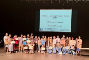 Camp participants on stage, standing in front of projected slide reading "Chinese Learning Summer Camp 2024 The School of Education