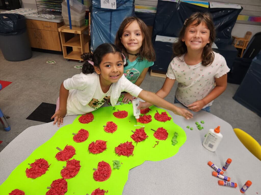 Three young girls smiling and crafting a poster together