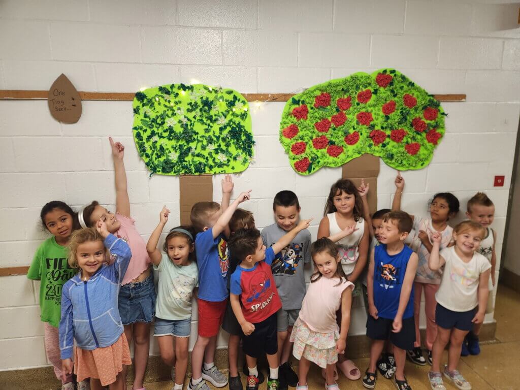 A class of children smiling together in front of two paper tree posters they have made.