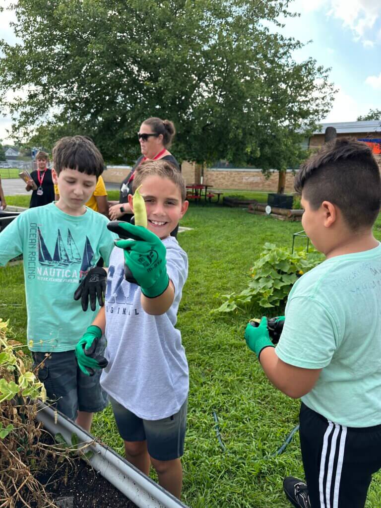 A child holding a green bean he grew and smiling.