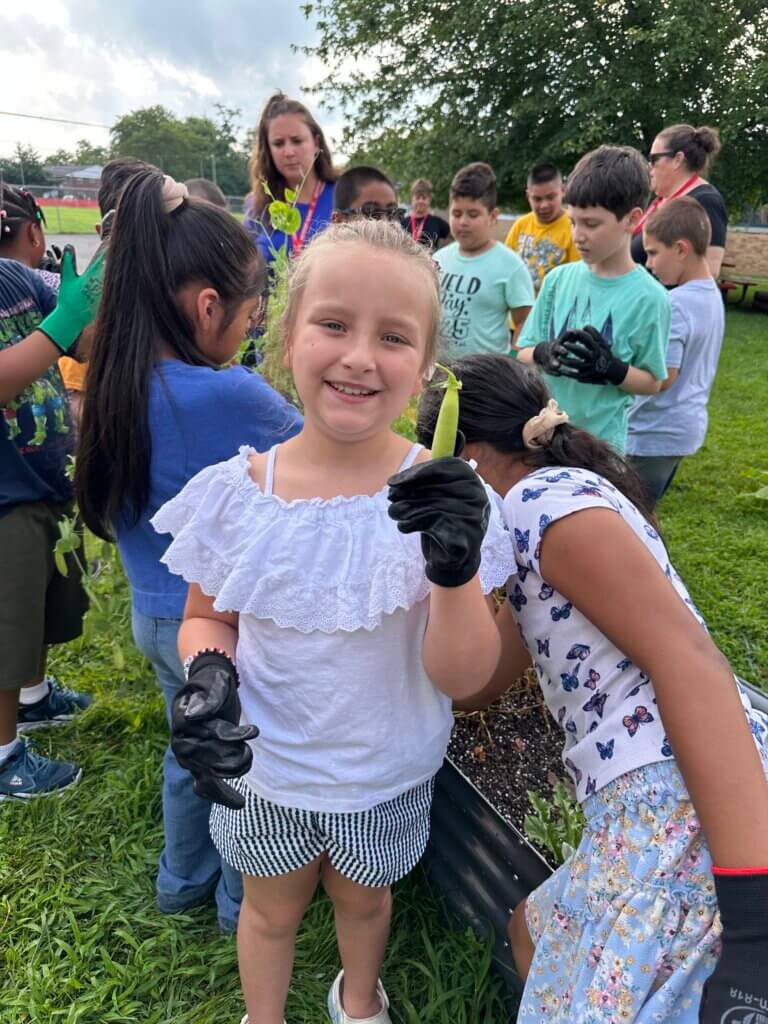 A child holding a green bean she grew and smiling.