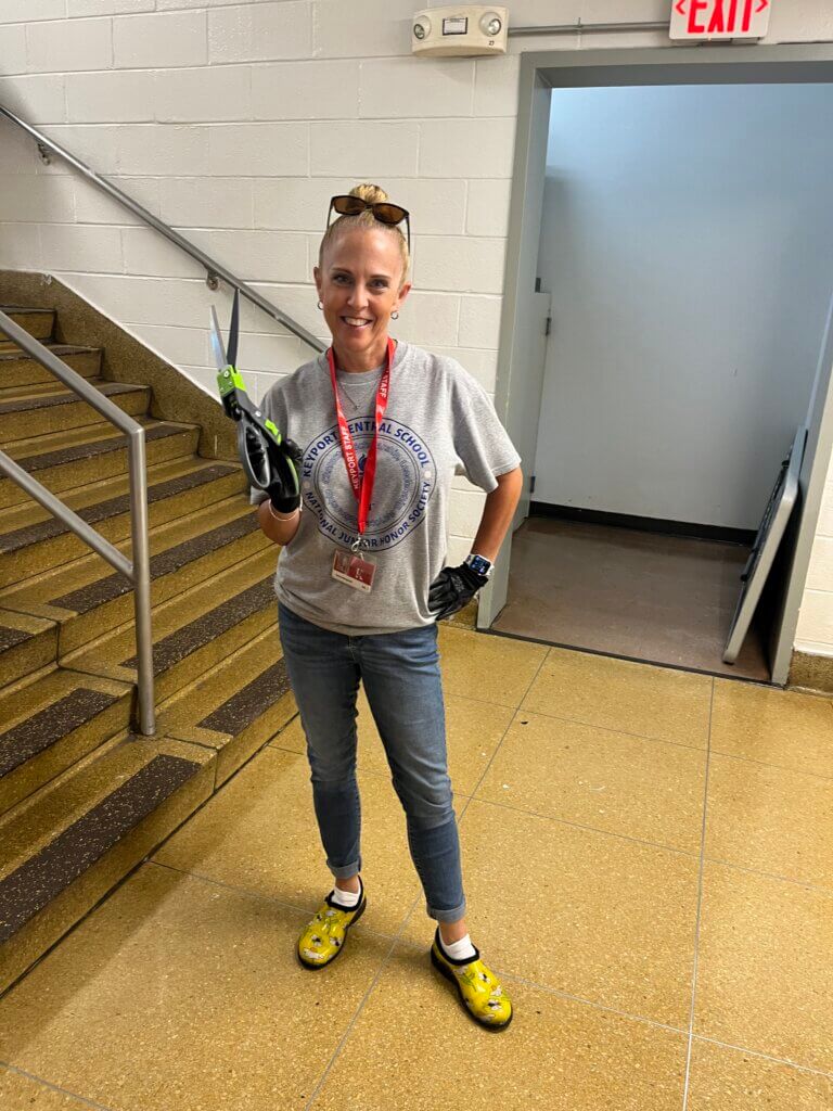 A teacher holding gardening tools.