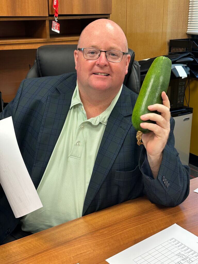 A faculty member holding a zucchini.
