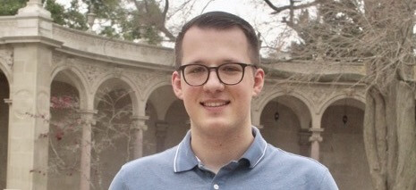 A white man wearing glasses photographed in front of a collonade.