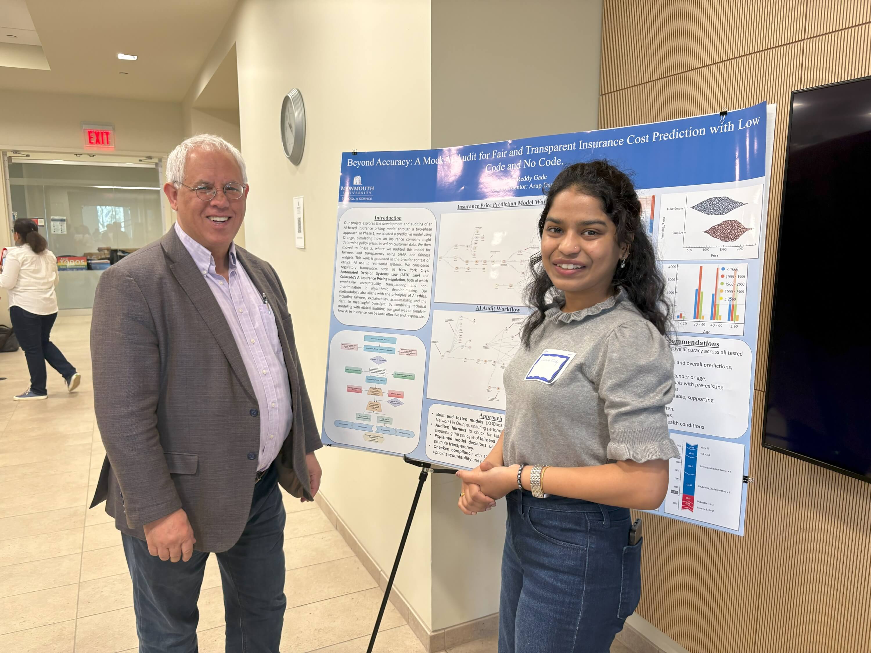 a professor and a student smile in front of her poster