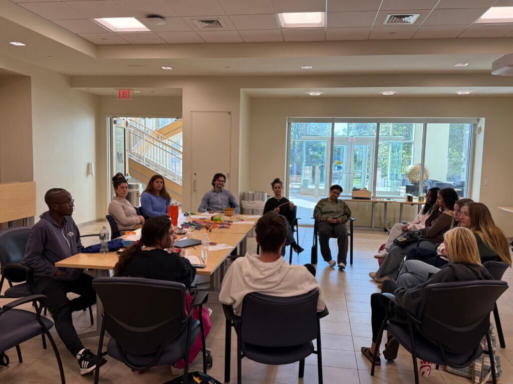 A group of people sit around a long desk, discussing some topic. 