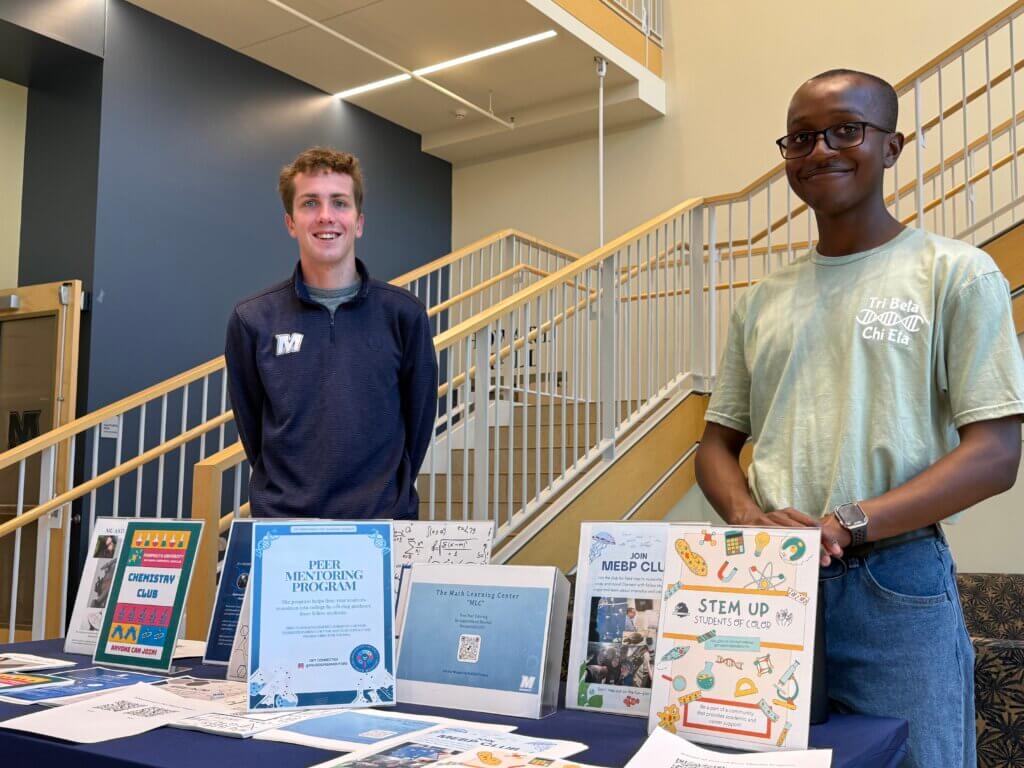 Two man standing in front of table with many club flyers.