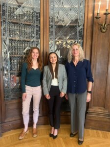 Three professional women standing in front of two cabinets filled with books