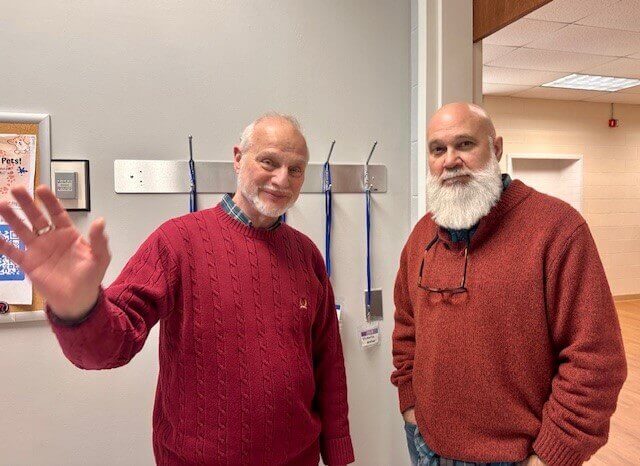 Two men in red sweaters smiling for the camera, one of whom is waving