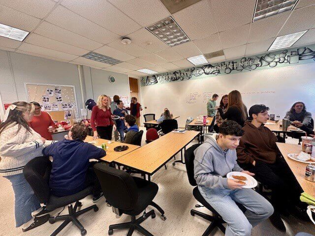 Gathering of students and professors eating together in a classroom.